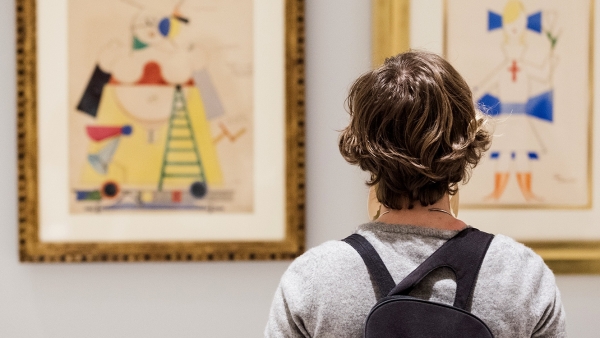 A student with his back to the viewer studies two brightly colored paintings in front of him.