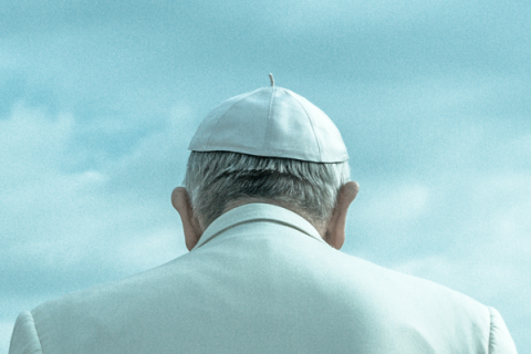 Pope Francis dressed in white, including a white cap, pictured from behind.