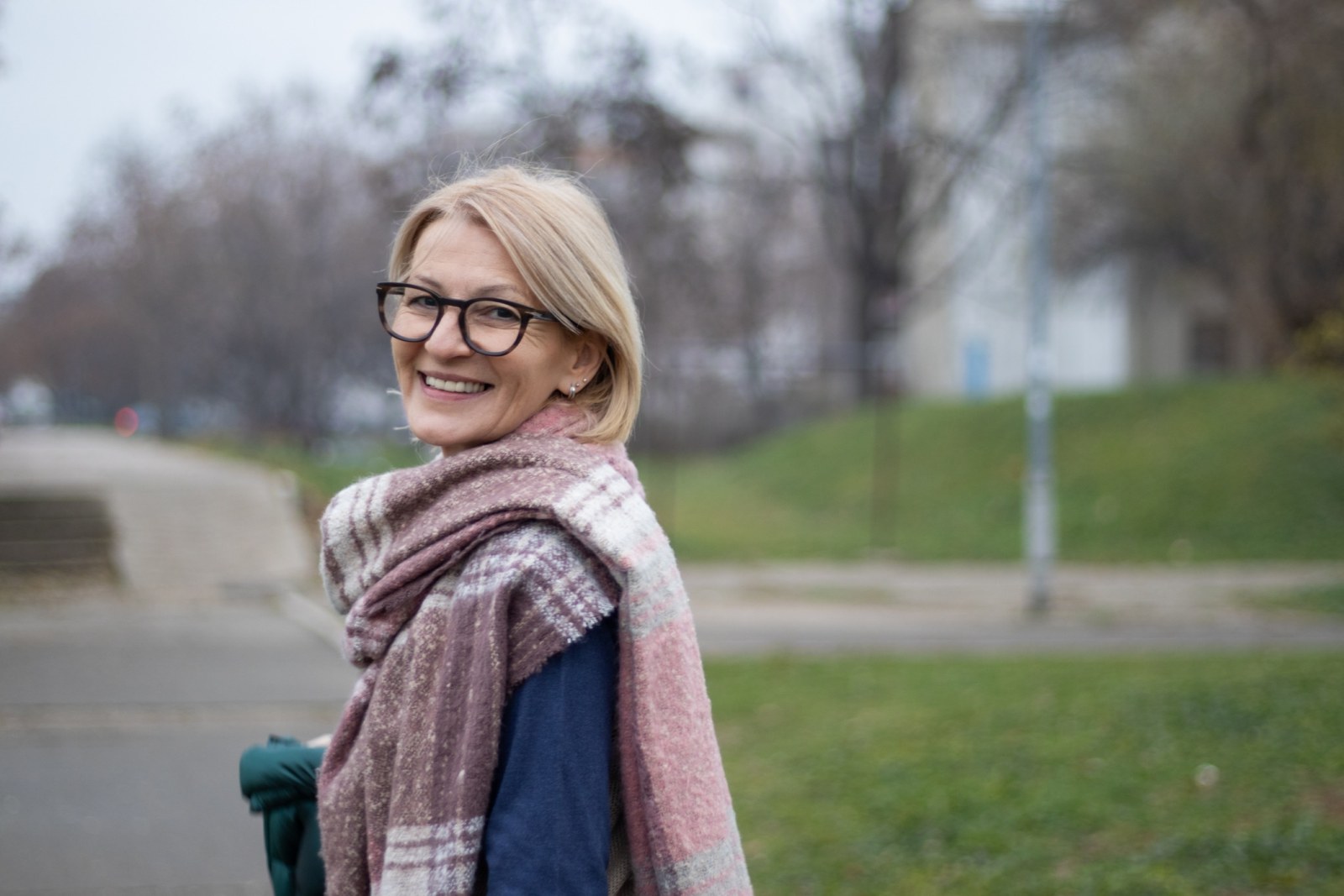 portrait of a mature blond woman with glasses in a city park on a winter day walking and looking cheerfully at the camera